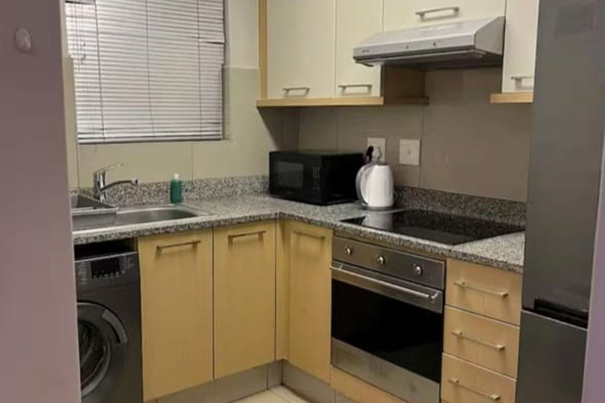 A compact, functional kitchen featuring light wood cabinetry, granite countertops, integrated oven and hob, and tiled flooring with a window for natural light.