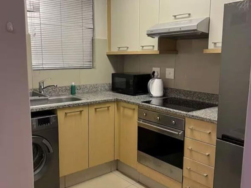 A compact, functional kitchen featuring light wood cabinetry, granite countertops, integrated oven and hob, and tiled flooring with a window for natural light.