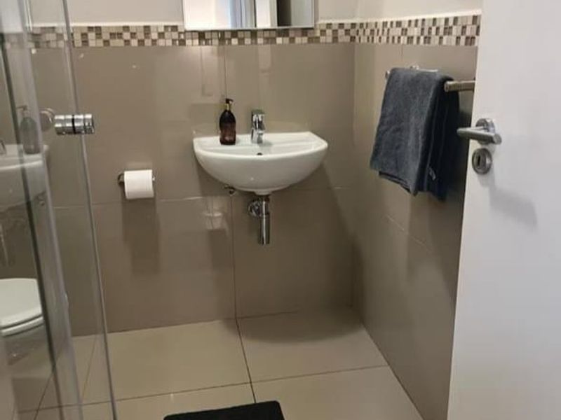 A compact, modern bathroom featuring a wall-mounted basin, glass shower enclosure, and neutral ceramic tiling with a decorative mosaic border.