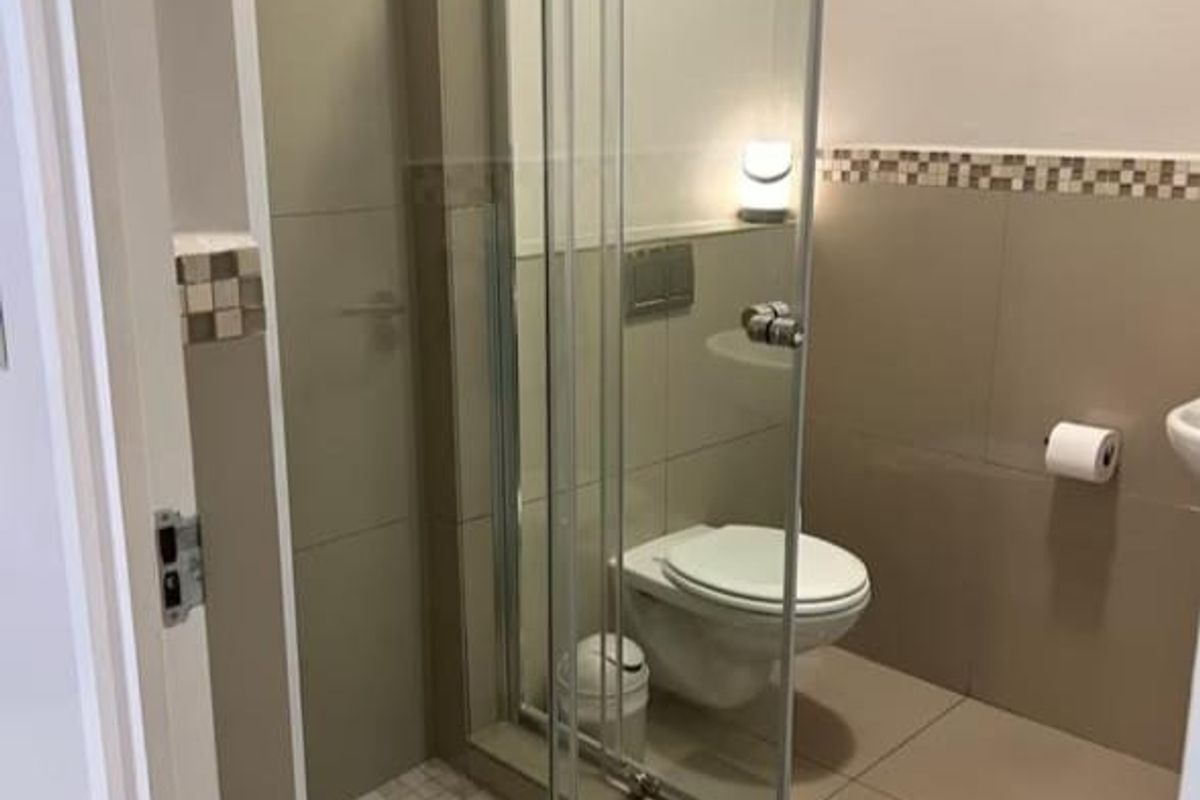 A modern bathroom featuring a glass-enclosed shower, wall-mounted toilet, and neutral-toned tiling with a decorative mosaic border.