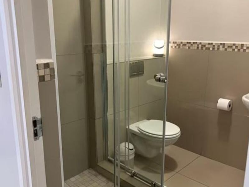 A modern bathroom featuring a glass-enclosed shower, wall-mounted toilet, and neutral-toned tiling with a decorative mosaic border.