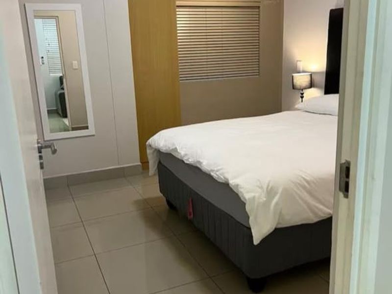 A well-maintained bedroom featuring neutral tiled flooring, built-in cabinetry, and venetian blinds, offering a clean and functional living space.