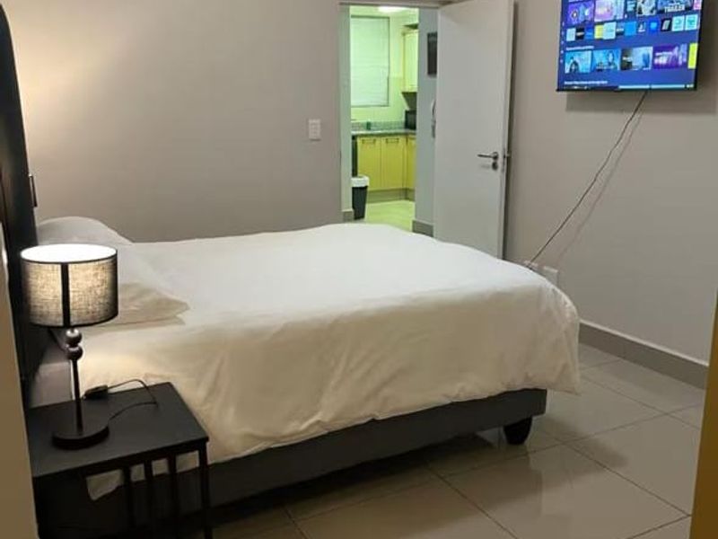 A well-maintained bedroom featuring neutral wall tones, tiled flooring, and coved ceiling details, with direct access to an adjacent kitchen area.
