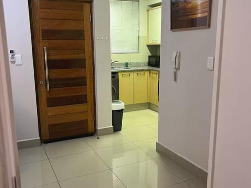 Entrance foyer featuring tiled flooring and an air conditioning unit, leading into a functional kitchen area with built-in cabinetry.