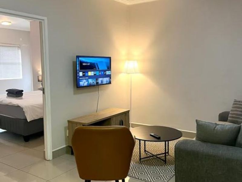 A well-maintained living room featuring neutral tiled flooring, cove ceiling detailing, and a modern flush mount light fixture, with an adjacent bedroom visible.