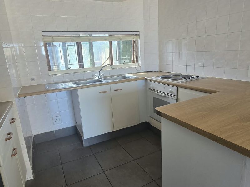 A functional kitchen featuring built-in cabinetry, a stainless steel sink, an electric hob, and an oven with tiled splashbacks and flooring.