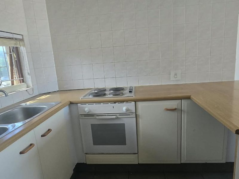 A functional kitchen featuring a double bowl stainless steel sink, built-in oven, electric hob, and ample laminate countertop space with tiled splashbacks.