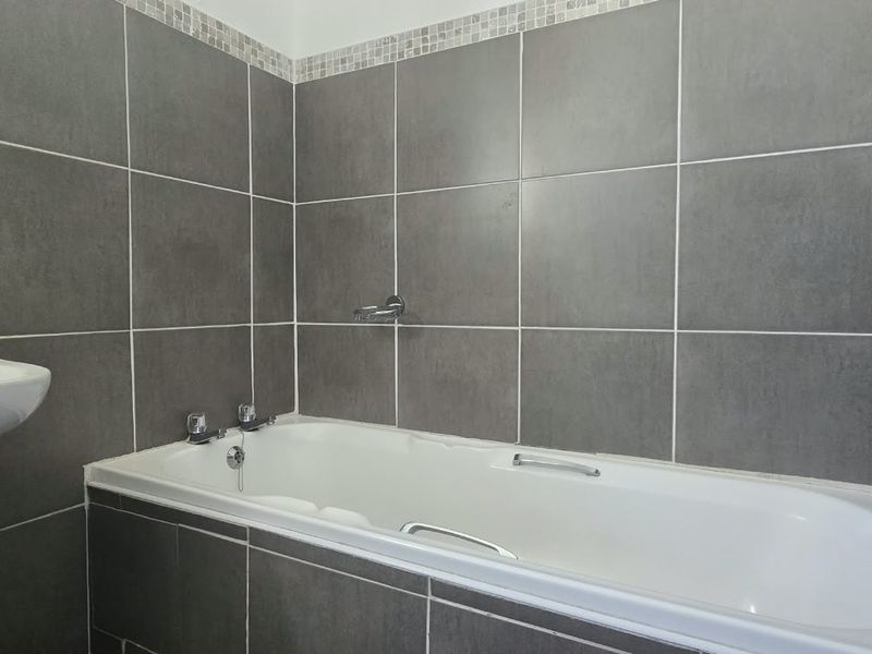 A clean bathroom featuring a pedestal basin and a built-in bathtub with modern grey wall tiling and chrome fixtures.