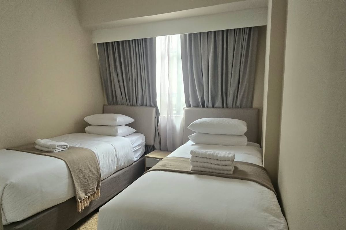 A compact bedroom featuring a neutral color palette, recessed window area with fitted curtains, and space for two single beds.