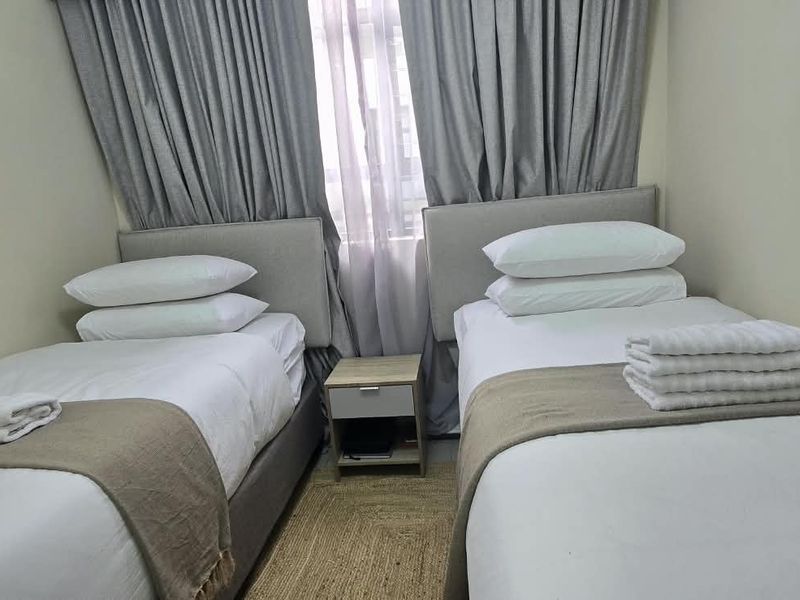A compact bedroom featuring two single beds positioned against a window with floor-to-ceiling curtains.