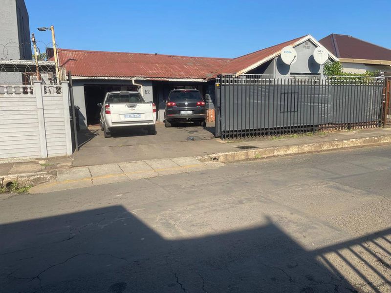 Front elevation of a residential property featuring a corrugated metal roof, perimeter fencing, and a concrete driveway with off-street parking.