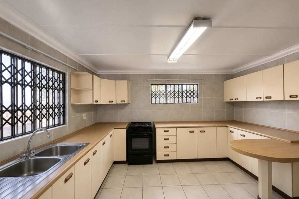 A functional, empty kitchen featuring tiled walls and flooring, ample built-in cabinetry, a double basin sink, and a freestanding stove.