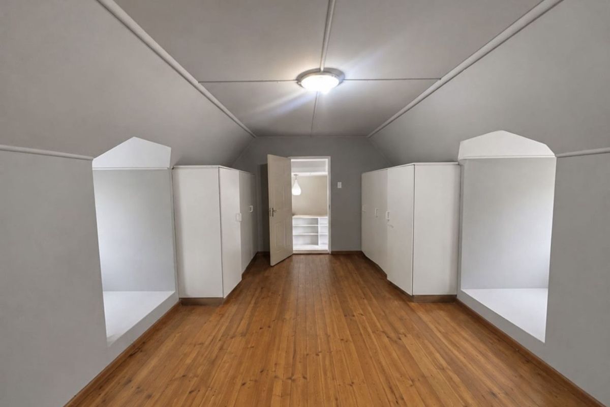Spacious attic-style bedroom featuring polished timber flooring, built-in cupboards, and unique dormer window alcoves under a vaulted ceiling.