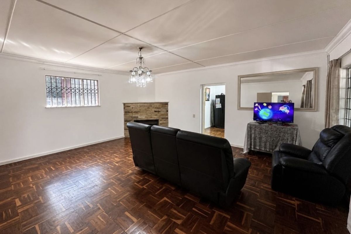 Spacious living room featuring classic parquet flooring, a stone fireplace, and a decorative crystal chandelier, offering a warm and traditional atmosphere.