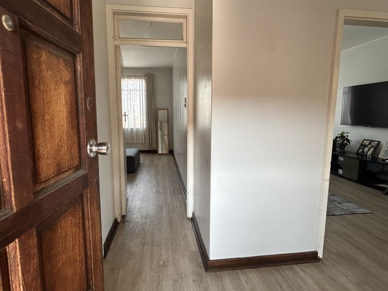 A functional hallway featuring laminate flooring and a traditional timber entrance door, providing access to adjacent living and bedroom areas.