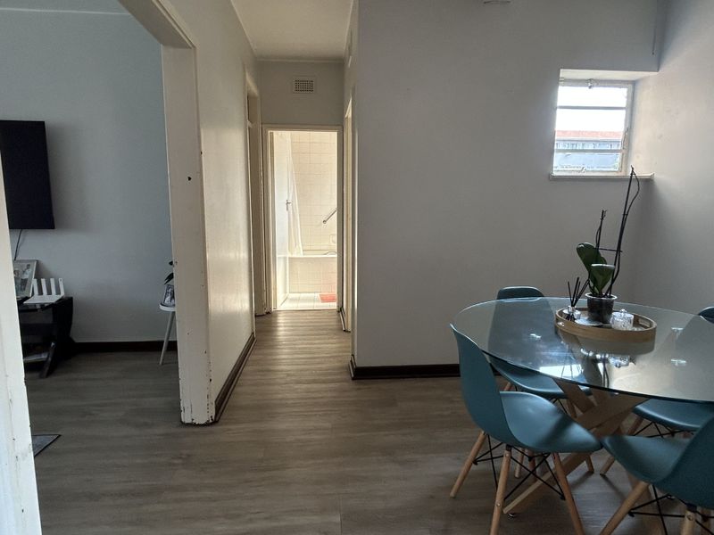 A view from the dining area looking through to the living room and bathroom, featuring laminate flooring and neutral wall finishes.