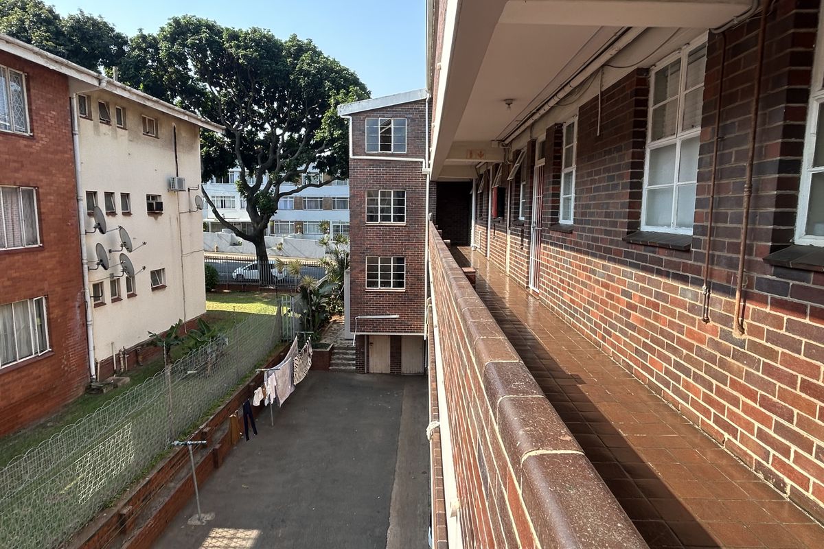 An elevated view of an apartment complex exterior, featuring a brick walkway, paved courtyard, and surrounding residential building facades.