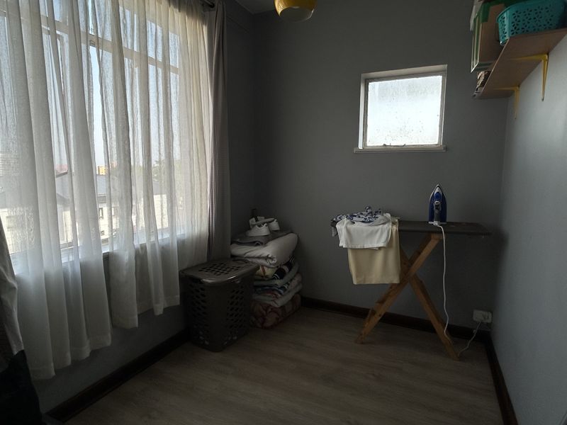 A functional laundry room featuring laminate flooring, large windows for natural light, and neutral wall finishes.