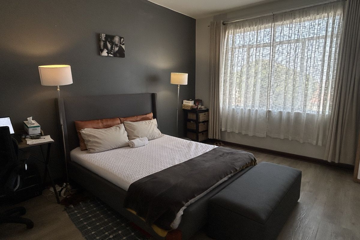 A well-maintained bedroom featuring laminate flooring, a ceiling fan, and large windows with curtain tracks, providing a comfortable and functional living space.