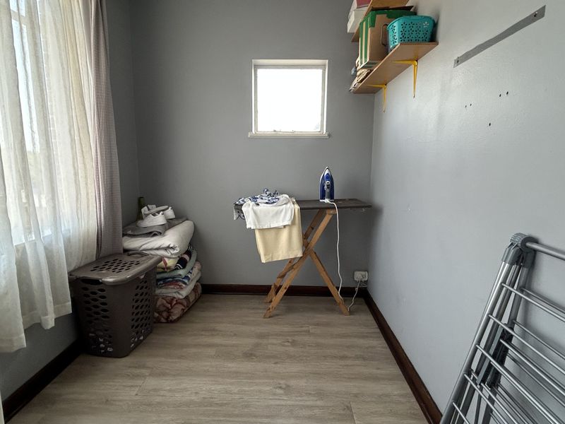 A functional laundry or utility room featuring laminate flooring, wall-mounted shelving, and a window for natural light.