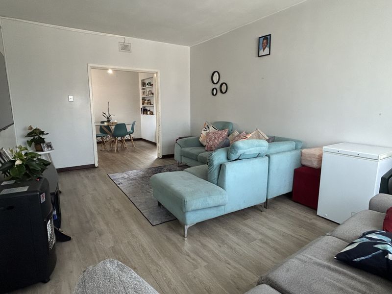 A spacious living room featuring light-toned laminate flooring and an open-plan transition to an adjacent dining area with built-in shelving.