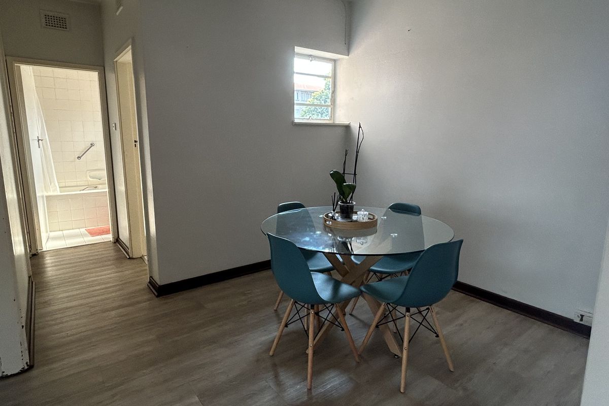 A simple living area featuring light-toned laminate flooring and neutral walls, with a clear view into the adjacent bathroom.