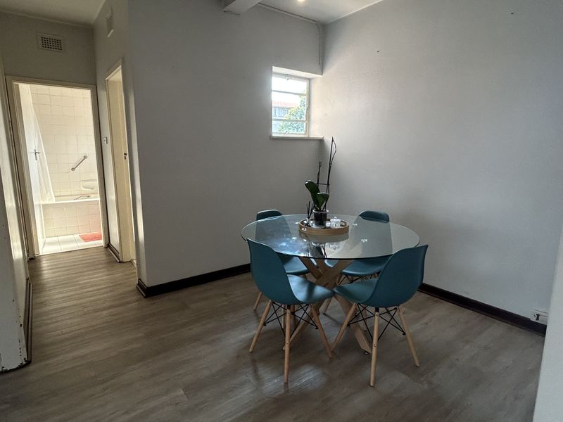 A simple living area featuring light-toned laminate flooring and neutral walls, with a clear view into the adjacent bathroom.