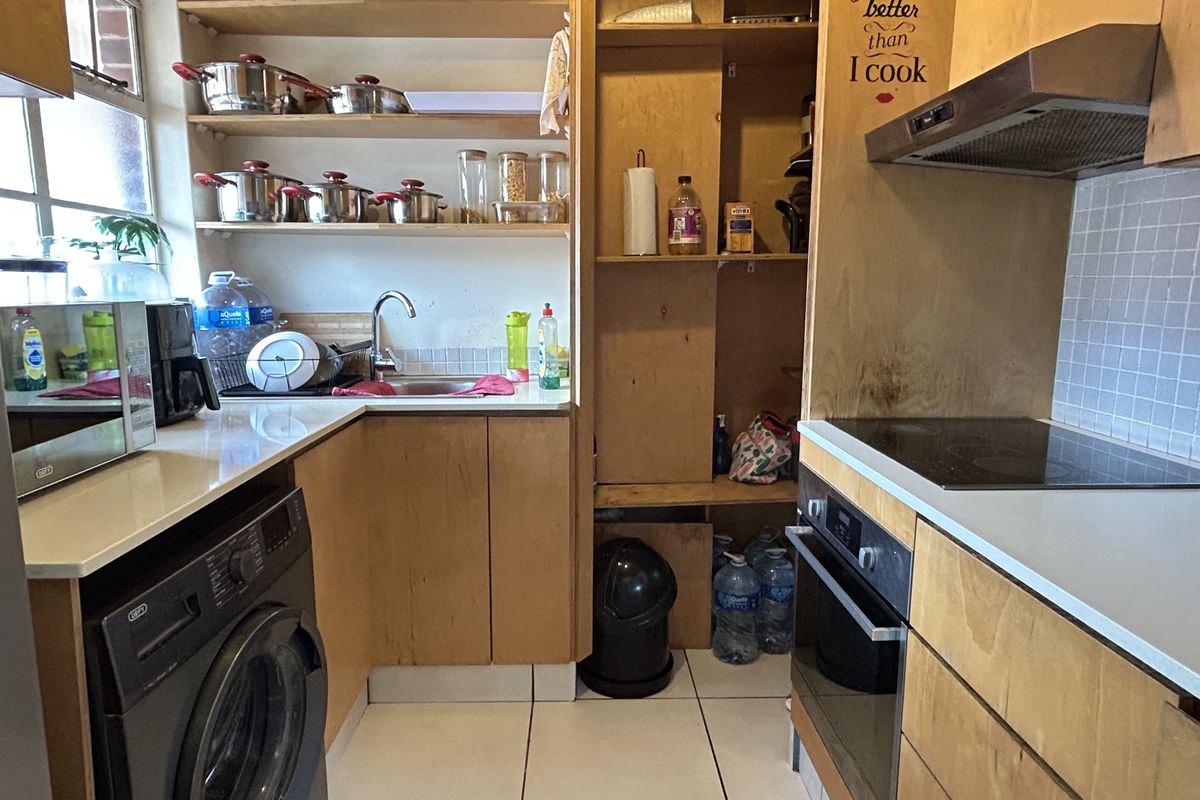 Compact kitchen featuring light wood cabinetry, built-in oven, electric hob, extractor fan, and tiled splashback with open shelving storage.