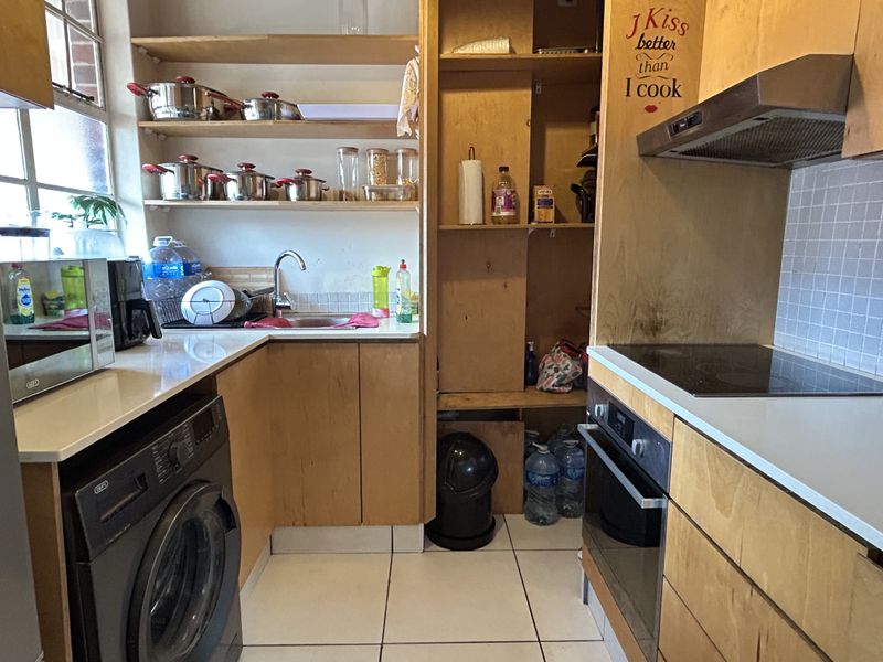 Compact kitchen featuring light wood cabinetry, built-in oven, electric hob, extractor fan, and tiled splashback with open shelving storage.