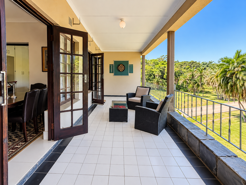 Spacious covered balcony featuring tiled flooring, metal balustrades, and direct access to the interior through classic french doors, overlooking a lush garden.
