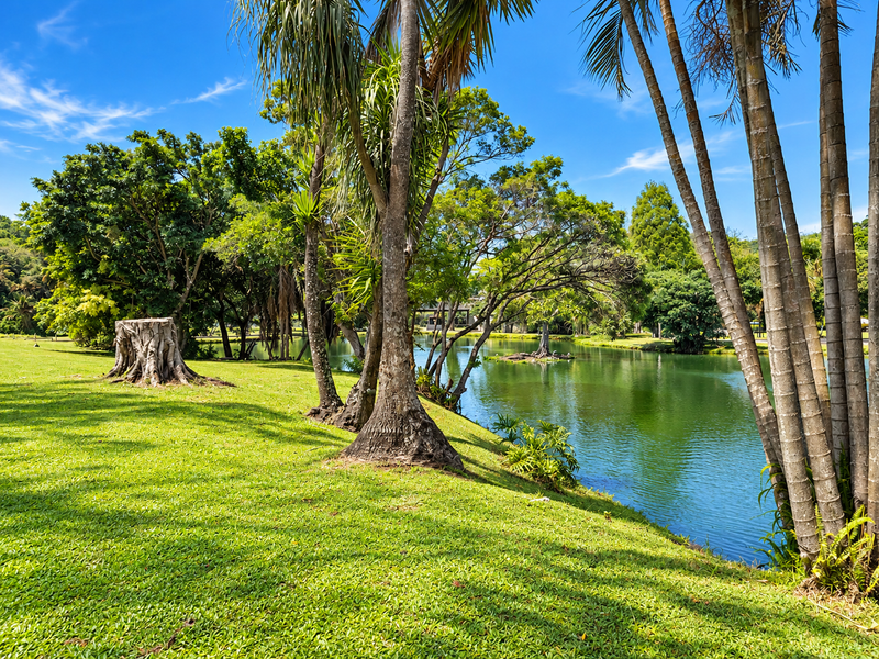 A scenic view of a well-maintained garden featuring a lush green lawn, mature trees, and a tranquil pond.