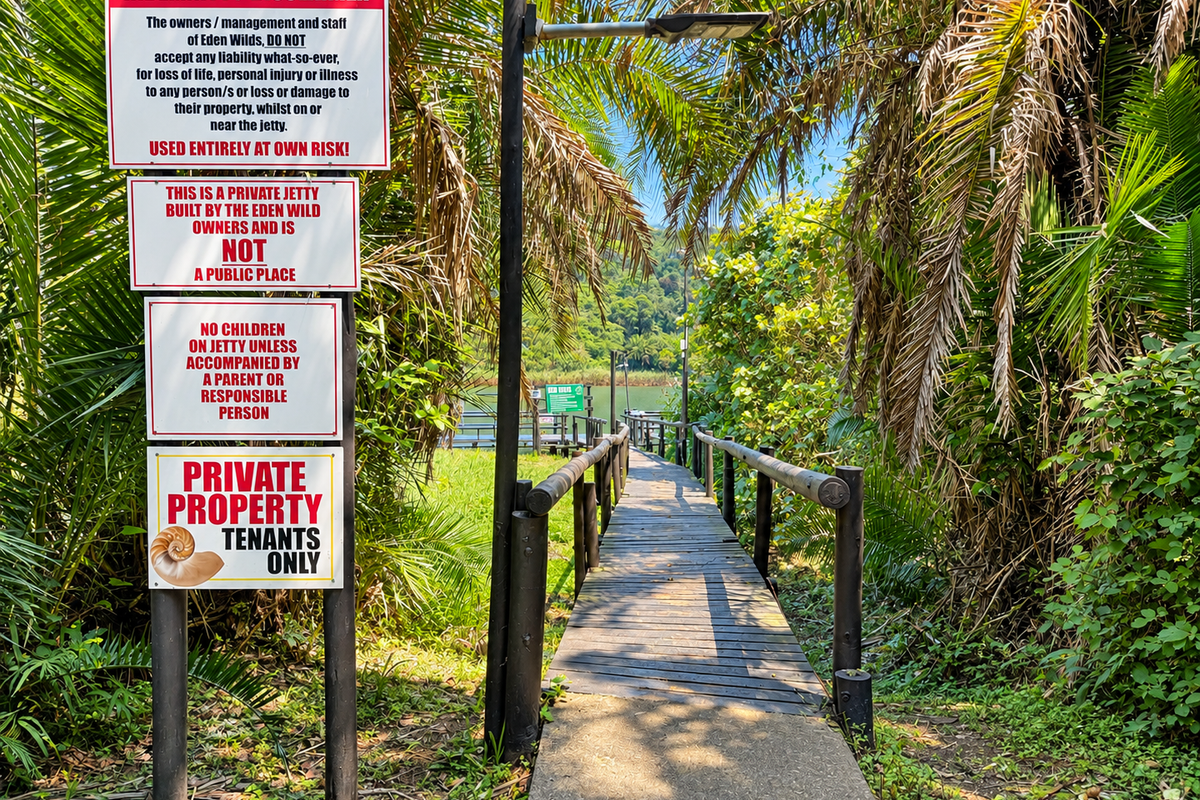 A private wooden jetty pathway leading towards the water, surrounded by lush vegetation and marked with property signage.