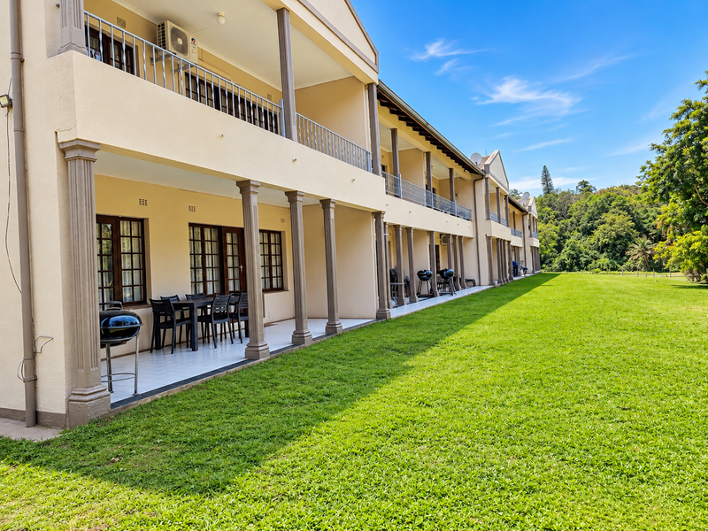 Rear view of a multi-story apartment complex featuring covered ground-floor patios and upper-level balconies overlooking a large, well-maintained lawn.