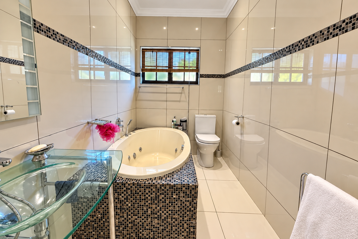 Modern bathroom featuring a built-in bathtub with mosaic tile surround, glass vanity, and neutral wall-to-wall ceramic tiling.