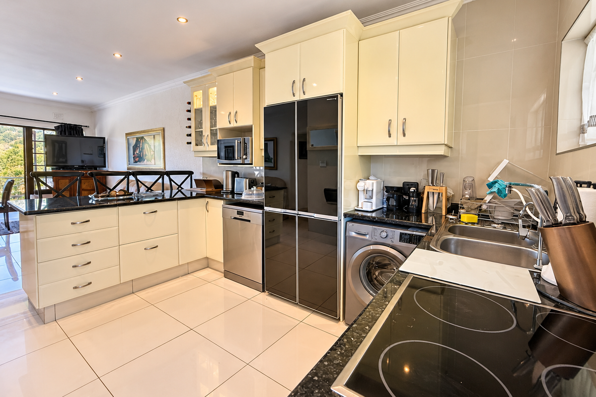 Modern kitchen featuring cream cabinetry, granite countertops, integrated appliances, electric hob, and tiled flooring, seamlessly flowing into the adjacent living area.