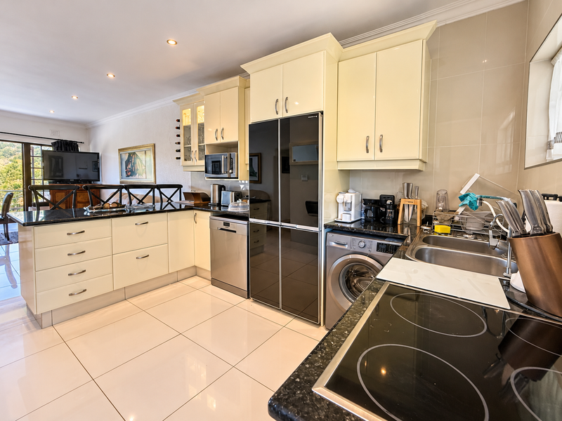 Modern kitchen featuring cream cabinetry, granite countertops, integrated appliances, electric hob, and tiled flooring, seamlessly flowing into the adjacent living area.
