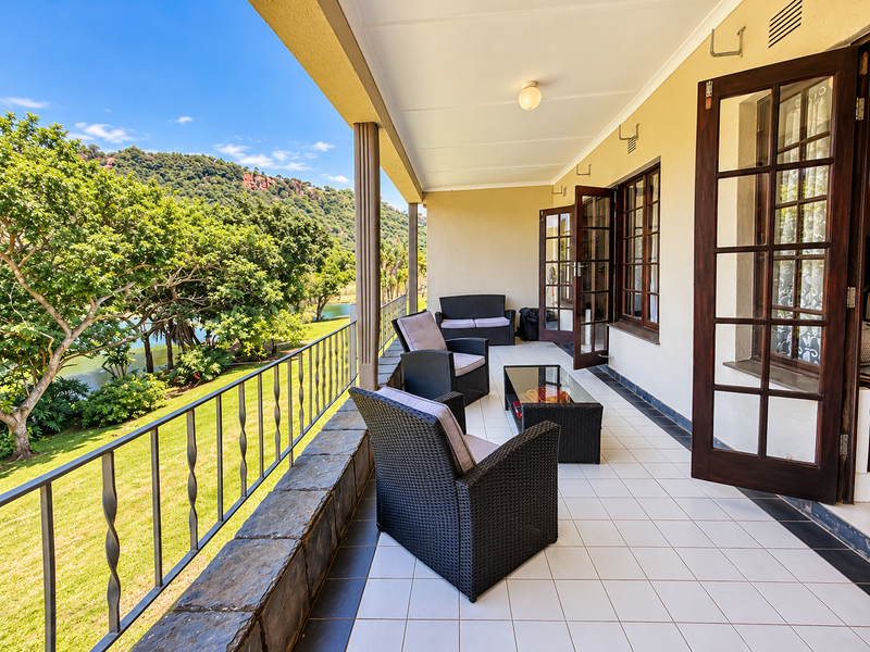 A spacious covered balcony featuring tiled flooring, wrought iron railings, and scenic views of the surrounding landscape and lake.
