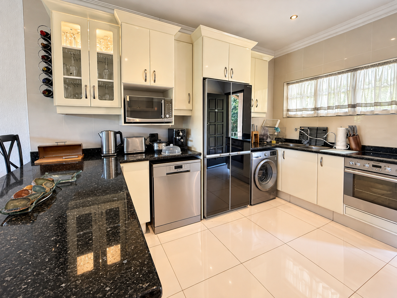 Modern kitchen featuring high-gloss cabinetry, granite countertops, integrated appliances, and polished ceramic tile flooring, offering a clean and functional culinary space.