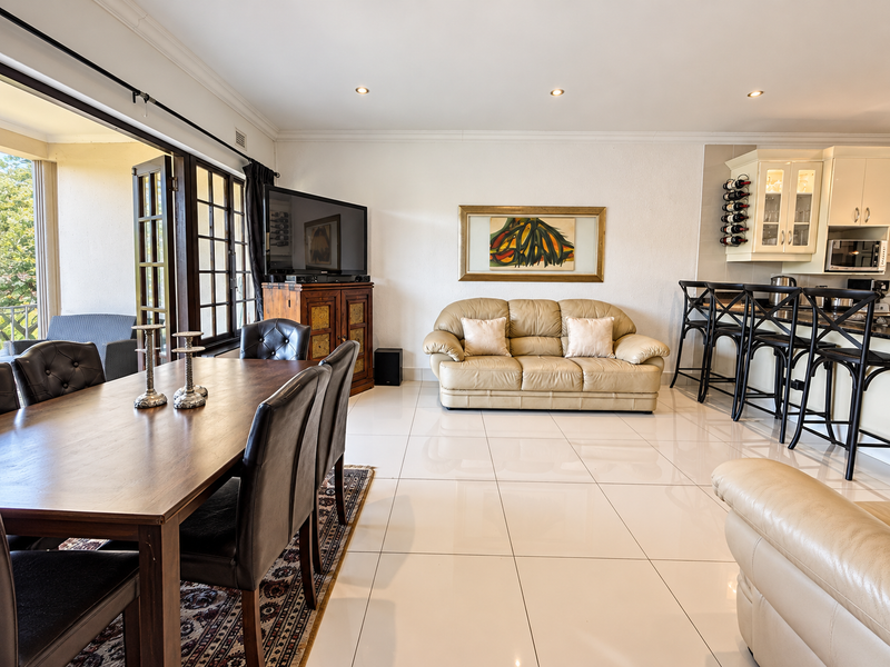 Spacious open-plan living and dining area featuring polished tile flooring, recessed lighting, and seamless access to an outdoor balcony through sliding glass doors.
