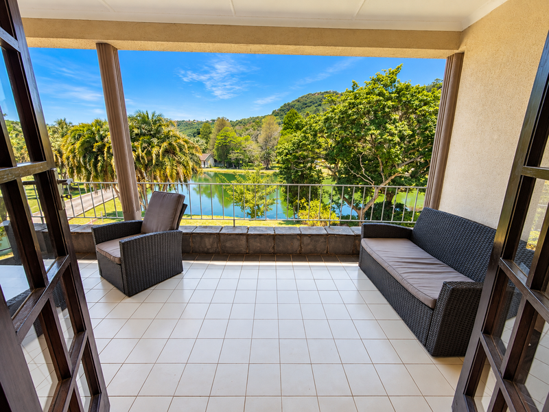 A covered balcony featuring tiled flooring and a metal balustrade, offering scenic views of the surrounding landscape and lake.