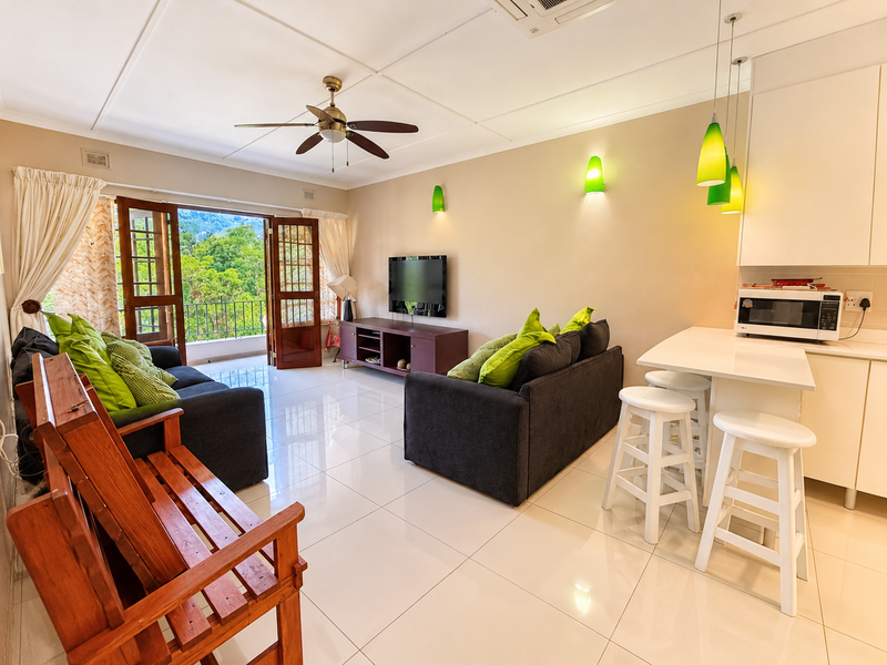 An open-plan living and kitchen area featuring tiled floors, modern cabinetry, built-in appliances, and french doors opening to a balcony with scenic views.