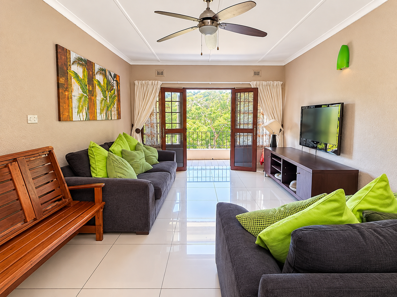 A bright and well-maintained living room featuring polished tiled floors, a ceiling fan, and double doors opening onto a balcony with scenic views.
