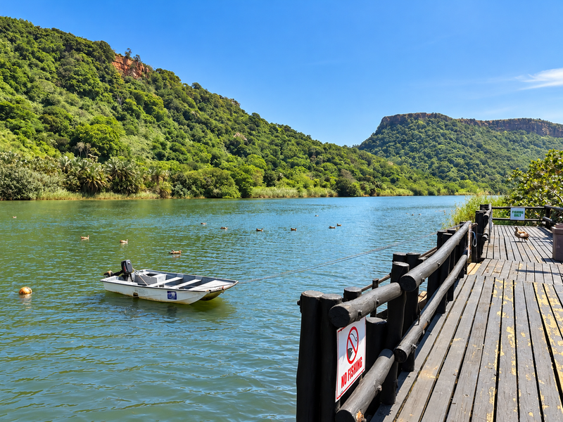 Scenic view of a river and surrounding hills from a wooden jetty with timber decking and railing.