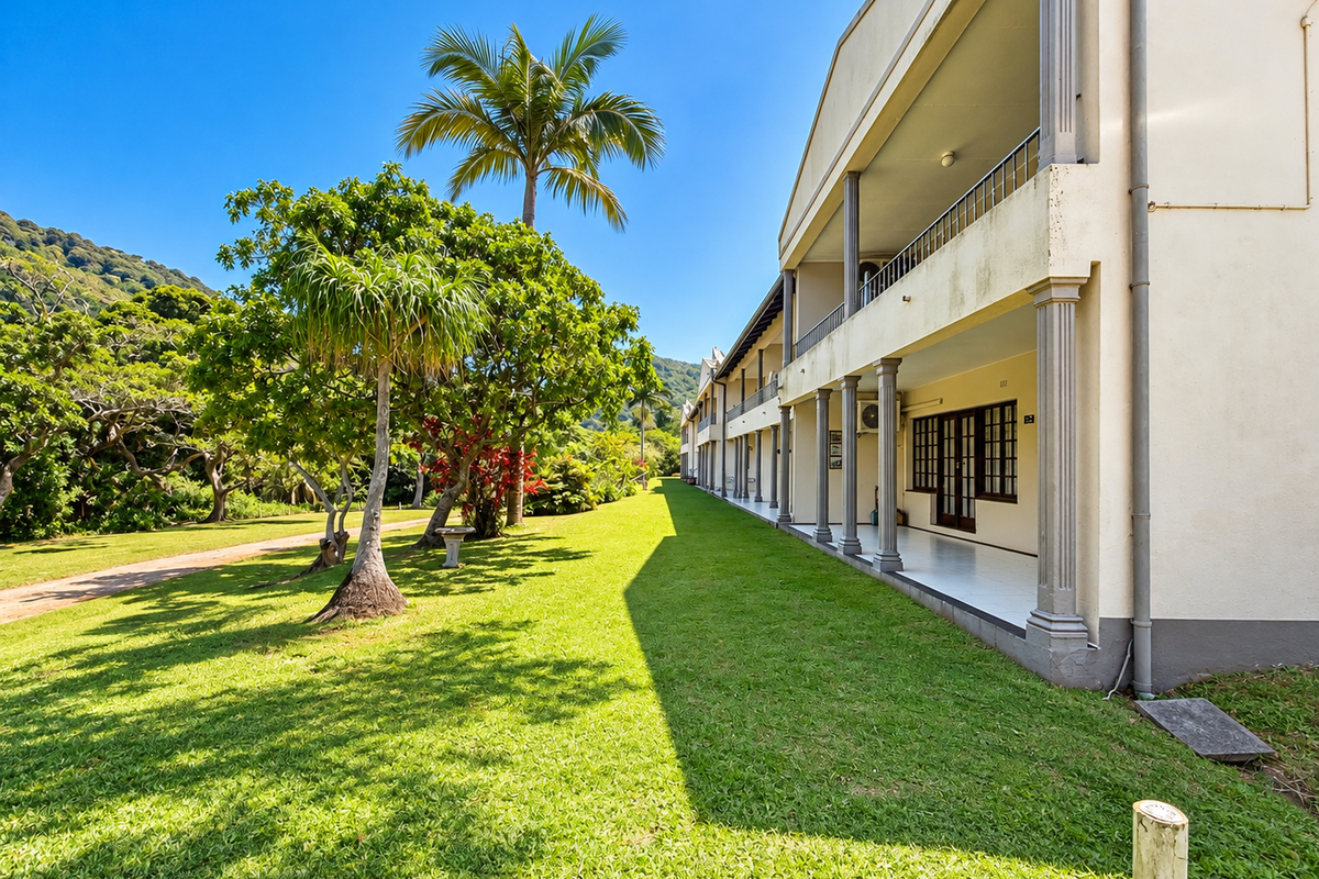 Exterior view of an apartment building featuring a covered ground-floor patio, upper-level balcony with railings, and a well-maintained garden area.
