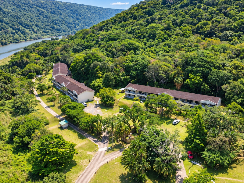 Aerial view of a residential apartment complex situated in a lush, green landscape with direct river frontage and extensive natural surroundings.
