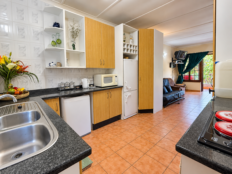 Open plan kitchen and living area featuring laminate cabinetry, double bowl sink, and ceramic tile flooring, leading to an outdoor patio space.