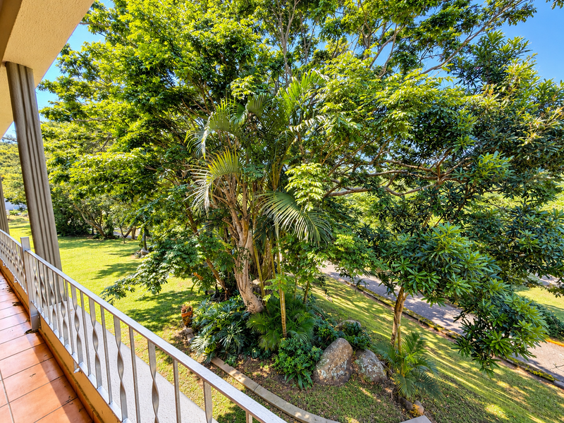 A balcony featuring tiled flooring and a metal balustrade, offering a pleasant view of the surrounding lush garden and mature trees.