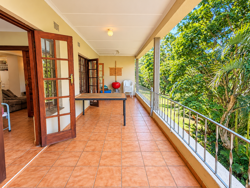 Spacious covered balcony featuring tiled flooring, metal balustrade, and direct access to the interior through multiple sets of wooden french doors.