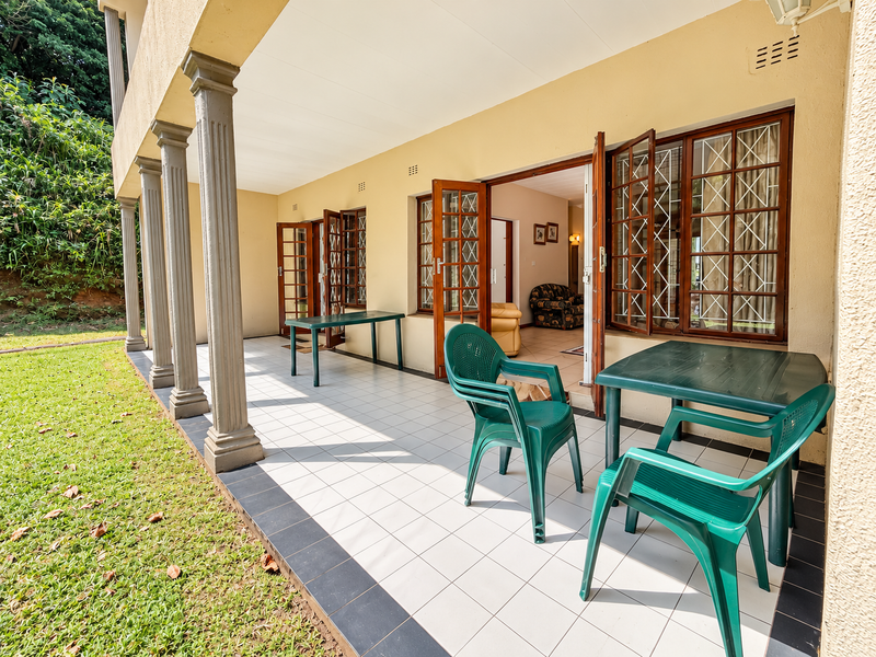 A covered patio area featuring tiled flooring, decorative columns, and multiple timber-framed doors providing access to the interior living space.