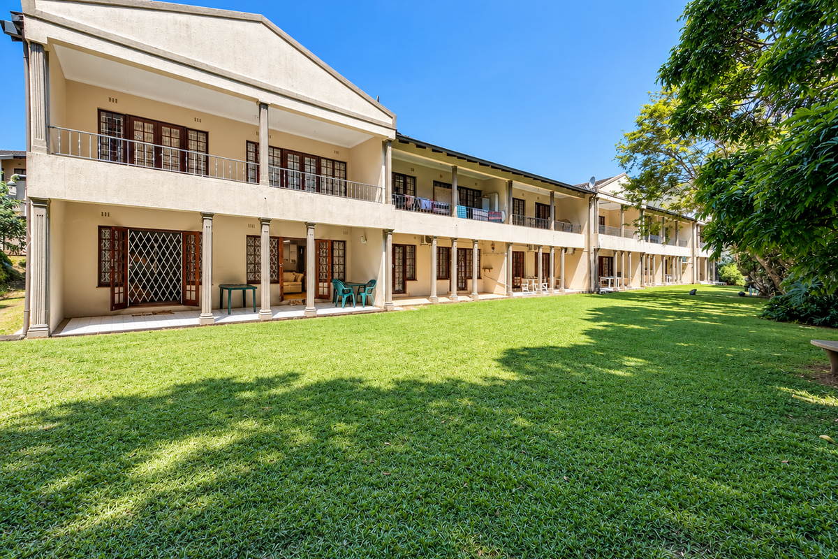 Rear view of a multi-story apartment complex featuring covered ground-floor patios, upper-level balconies with metal railings, and a well-maintained communal lawn area.